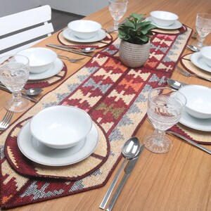 Puede incluir: Una mesa puesta con un camino de mesa estampado en rojo, naranja y beige. El camino de mesa está rodeado de platos, cuencos y vasos blancos. También hay tenedores y cucharas de plata en la mesa.