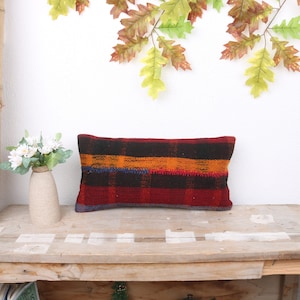 May include: A rectangular pillow with a red, orange, black, and blue plaid pattern. The pillow is sitting on a wooden table.