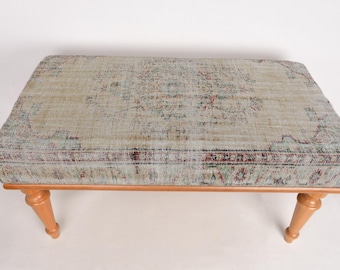May include: A light brown wooden bench with a floral patterned rug top. The rug has a light beige background with a darker beige floral pattern.
