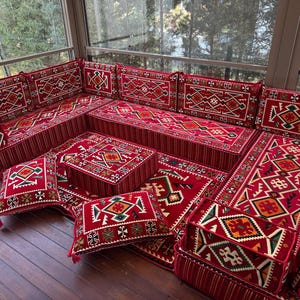 May include: A red and white patterned floor seating set with cushions and a coffee table. The set is made of fabric and has a traditional design.