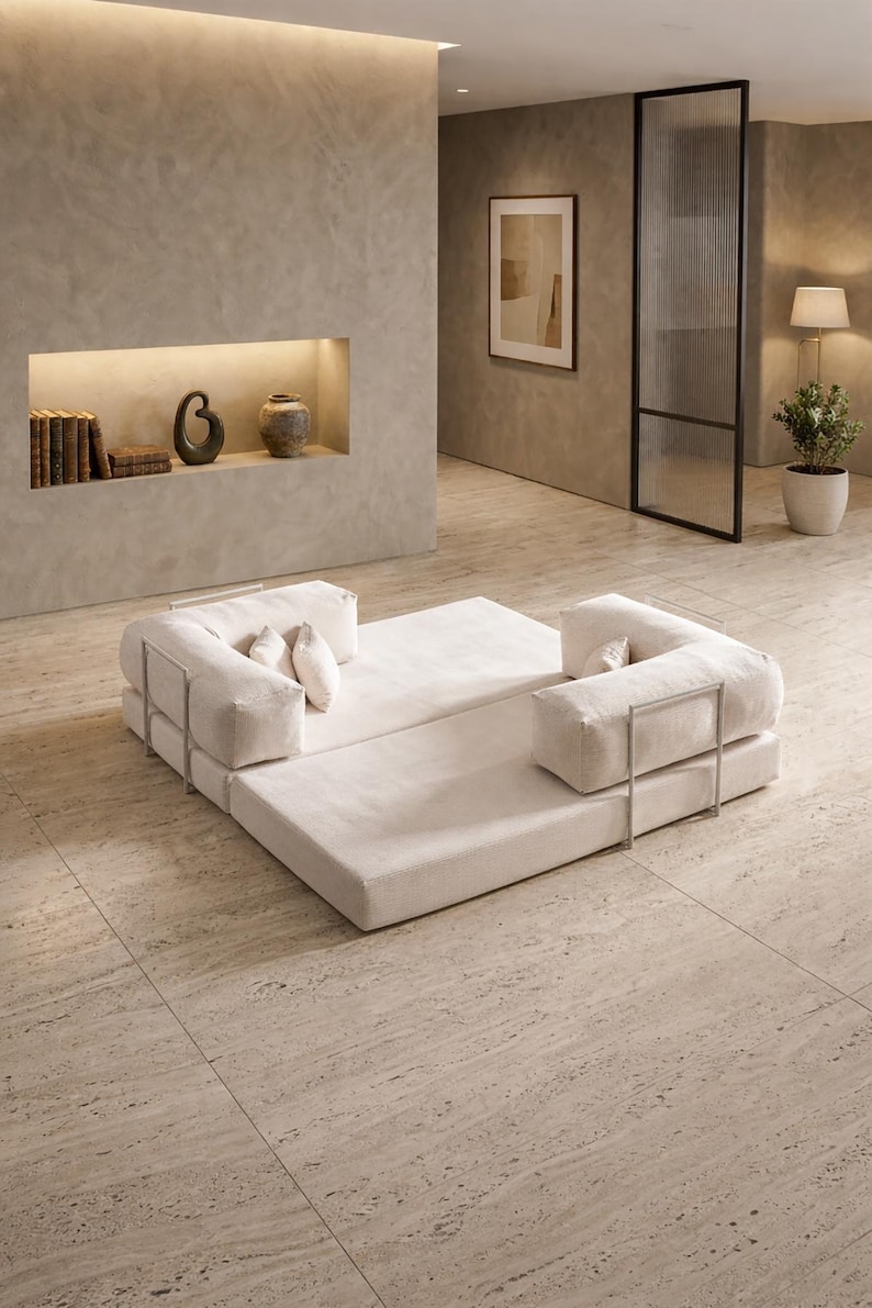 May include: Modern modular sofa in a neutral color palette. The sofa features a low profile design with a rectangular base and two L-shaped seating sections. The sofa is accented with metal frames and includes several throw pillows. The room has a minimalist design.