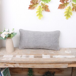 May include: A gray rectangular pillow with a textured surface sits on a wooden table. The table has a rustic look with knots and grain visible.