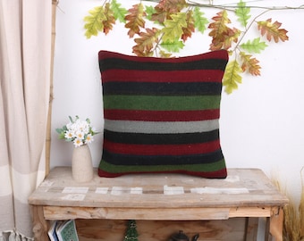 May include: Striped throw pillow with red, green, black, and gray stripes. The pillow is made of a soft, woven fabric and has a square shape.