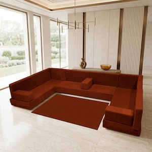 May include: A large U-shaped sectional sofa upholstered in a rust-colored corduroy fabric with a matching rectangular area rug positioned in the center. The sofa features a low-profile design with integrated armrests and a modular seating arrangement.