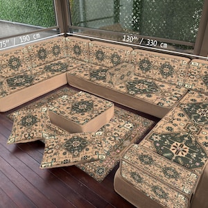 Può includere: Un set di divani modulari con base beige e cuscini fantasia. Il set comprende un divano angolare, un pouf e cuscini. Il divano misura 330 cm di lunghezza e 190 cm di larghezza. Il pouf è 70 cm.