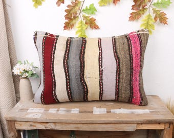 May include: A striped throw pillow with a variety of colors, including red, pink, beige, and gray. The pillow is made of woven fabric and has a rustic, hand-crafted look.