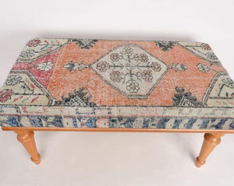 May include: A wooden bench with a colorful patterned cushion. The cushion has a traditional rug design with shades of red, blue, and white.