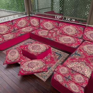 May include: A U-shaped sofa in red with an ornate floral design. The sofa, measuring 330 cm by 190 cm, includes matching cushions and an ottoman. The set is completed with a patterned rug and pillows. The sofa's height is 70 cm.