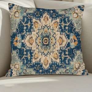 Könnte beinhalten: Ein quadratisches Zierkissen mit einem symmetrischen, komplizierten Medaillonmuster in den Farben Dunkelblau, Hellblau, Creme und gedämpftem Gold. Das Design zeigt ein zentrales sternförmiges Motiv, umgeben von verzierten floralen und geometrischen Rändern.