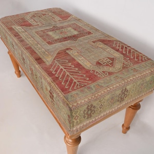 May include: A wooden bench with a red, green, and beige patterned fabric top. The bench has turned wooden legs.