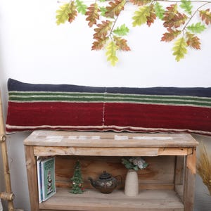 May include: A long, rectangular cushion with a striped design. The top section is navy blue, followed by a green stripe, and a burgundy red section. The cushion is placed on a wooden table.
