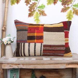 May include: A rectangular patchwork pillow with a brown, red, orange, and white design. The pillow is made of woven fabric and has a rustic, handmade look.
