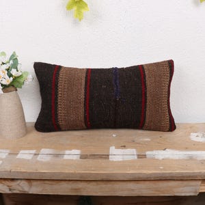 May include: A brown and black striped throw pillow with a woven texture. The pillow is on a wooden surface.