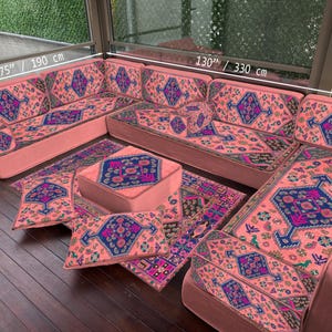 Puede incluir: Un sofá seccional de color coral con un diseño estampado en azul, morado y blanco. El sofá mide 330 cm por 190 cm e incluye cojines y una alfombra a juego. El conjunto está sobre un suelo de madera.