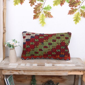 May include: A rectangular pillow with a colorful geometric pattern in shades of red, green, blue, and yellow. The pillow is made of woven fabric and has a fringed edge.