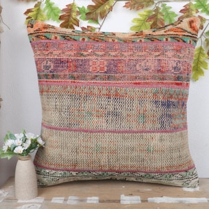 May include: A decorative pillow with a vintage, textured design. The pillow features a mix of colors including pink, purple, green, and beige. The pillow is rectangular and appears to be made of woven fabric, adding a touch of rustic charm to any space.