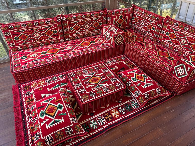 May include: A red and white patterned floor cushion set with intricate geometric designs. The set includes a large sofa-like cushion, smaller square cushions, and a rectangular rug. The cushions are arranged in a traditional Moroccan style.