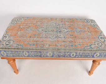 May include: A wooden bench with a colorful patterned rug top. The rug has a light orange background with blue, white, and pink floral designs.