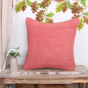 May include: A coral pink throw pillow with a textured woven fabric. The pillow is sitting on a wooden table.