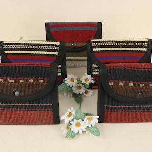 Könnte beinhalten: Fünf gewebte Stoffbeutel mit Klappenverschlüssen. Die Beutel weisen eine Mischung aus roten, schwarzen, braunen und blauen Farben mit gestreiften und geometrischen Mustern auf. Jeder Beutel hat einen schwarzen Rand und einen Knopfverschluss.