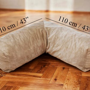 May include: A beige, corduroy-textured, L-shaped floor cushion. The cushion measures 43 inches long, 20 inches wide, and 13 inches high. The dimensions are labeled on the image. The cushion is placed on a wooden floor.