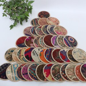 May include: A collection of 25 round, colorful coasters made from woven fabric with a beige border. The coasters are arranged in a triangular pattern on a white surface.