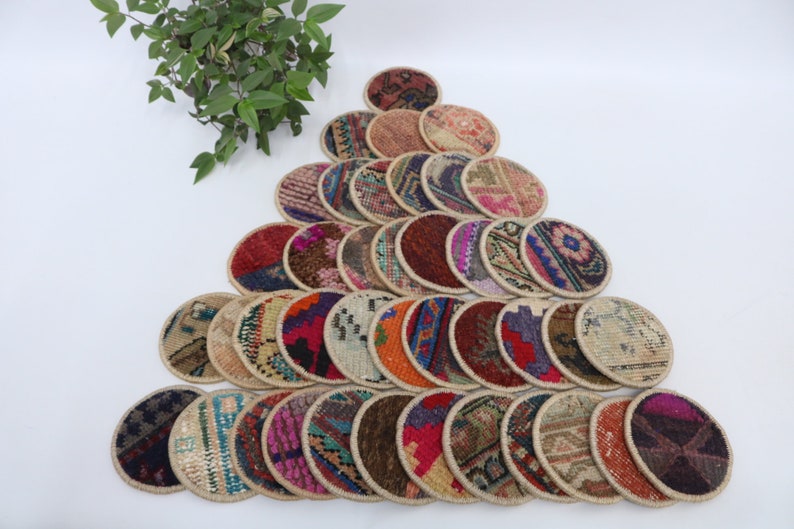 May include: A collection of 25 round, colorful coasters made from woven fabric with a beige border. The coasters are arranged in a triangular pattern on a white surface.