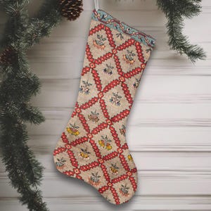 Può includere: Una calza di Natale con sfondo beige e motivo geometrico rosso e blu. La calza è decorata con motivi floreali gialli e blu. Un nastro bianco è attaccato per appenderla.