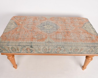May include: A wooden bench with a light brown finish and a patterned rug top. The rug has a light orange background with a darker orange and blue floral design.