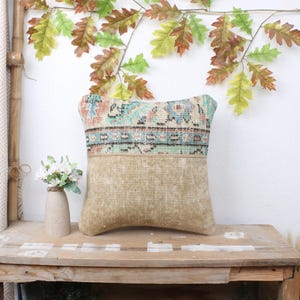 May include: A decorative throw pillow with a colorful patterned fabric on one side and a solid beige fabric on the other side. The pillow is sitting on a wooden table.