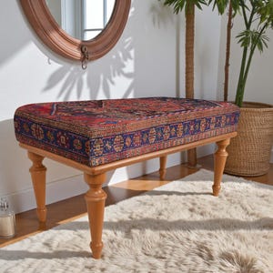 May include: A rectangular bench with a patterned, upholstered top in shades of red, blue, and brown. The bench has light brown, turned wooden legs. The bench is placed on a fluffy, white rug.