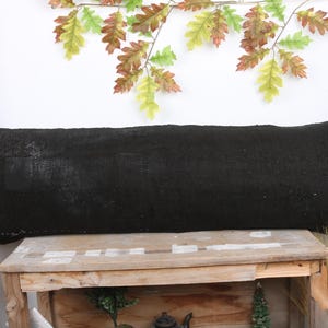 May include: A black, rectangular lumbar pillow resting on a wooden table. The pillow is made of a soft, textured fabric.