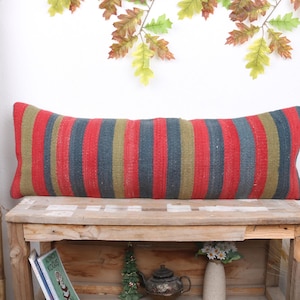 May include: A long, rectangular pillow with red, green, and blue stripes. The pillow is made of woven fabric and is resting on a wooden shelf.