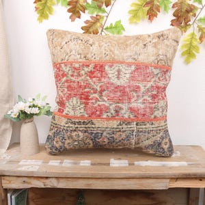 May include: A decorative throw pillow with a patchwork design featuring beige, red, and blue colors. The pillow is made from a vintage rug and has a frayed edge.