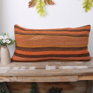 Puede incluir: Una almohada larga y rectangular con un patrón de rayas en tonos naranja, marrón y beige. La almohada está hecha de tejido tejido y tiene una superficie ligeramente texturizada.
