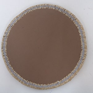 May include: A round, brown fabric patch with a light gray and beige stitched border.