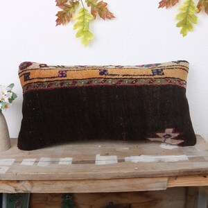 May include: A brown and beige patterned throw pillow with a dark brown background. The pillow has a fringe border and is sitting on a wooden table.