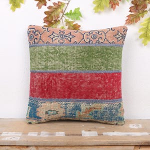 May include: A rectangular pillow with a patchwork design. The pillow features horizontal stripes of pink, green, and red, with blue patterned sections at the top and bottom. The pillow is placed on a wooden surface.