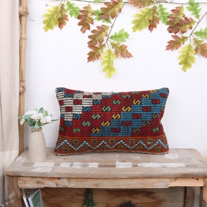May include: A rectangular pillow with a colorful geometric pattern in shades of red, blue, yellow, and white. The pillow is made of woven fabric and has a fringed edge.