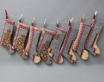 Puede incluir: Ocho calcetines de Navidad de colores con patrones colgados de una cuerda para tender la ropa. Los calcetines están hechos de una tela tejida con un fondo gris y patrones rojos, amarillos y blancos.