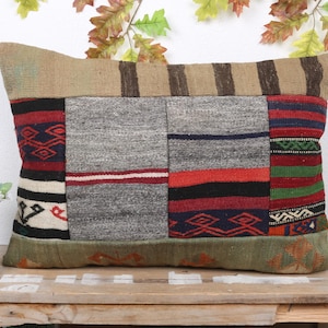 Puede incluir: Cojín decorativo rectangular con un diseño de patchwork. El cojín presenta una variedad de colores, incluyendo rojo, negro, gris y verde. El cojín está hecho de una tela tejida y tiene un aspecto texturizado. El cojín está colocado sobre una superficie de madera.