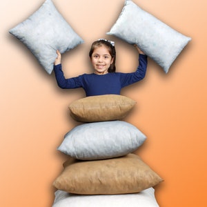 May include: A young girl is holding two white pillows above her head, while sitting on a stack of four pillows. The pillows are arranged in a pyramid shape, with two brown pillows in the middle and two white pillows on the top and bottom. The background is a gradient of orange and white.