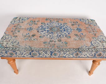 May include: A wooden ottoman with a colorful patterned rug top. The rug has a light pink background with blue and green floral designs.
