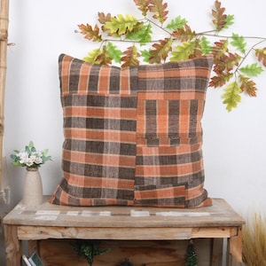 May include: A brown and orange plaid throw pillow with a patchwork design. The pillow is made of a soft, woven fabric and has a square shape.