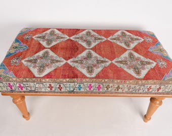 May include: A wooden ottoman with a red, white, and blue patterned cushion. The cushion has a geometric design with intricate details.