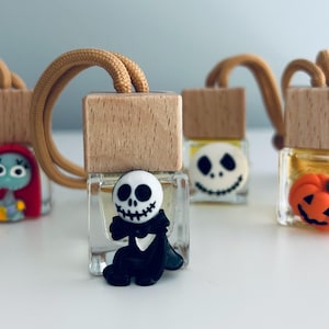 Könnte beinhalten: Fünf kleine Glasflaschen mit Holzdeckeln und bunten Figuren-Anhängern. Die Anhänger umfassen einen Kürbis, einen Schädel und eine Figur mit roten Haaren. Die Flaschen hängen an einer Schnur.