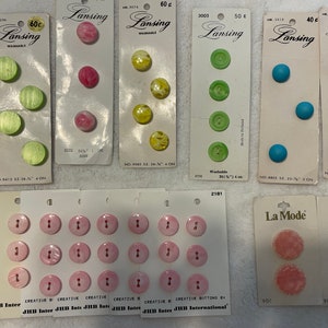 May include: Assortment of colorful plastic buttons in various sizes and shapes, packaged on cards with the brand names "Lansing" and "La Mode".