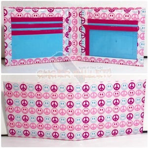 May include: A handmade wallet made of duct tape. The wallet is white with a pattern of pink peace signs and smiling faces. The interior features blue and pink accents, with card slots. The text "Made of Duct Tape" is visible.