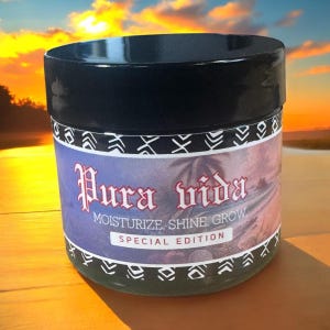 Puede incluir: Un tarro negro con una etiqueta verde y blanca que dice "Pura Vida Moisturize, Shine, Grow Special Edition". El tarro está sobre una superficie de madera.