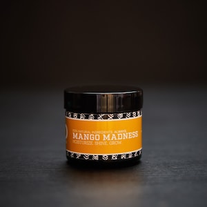 May include: A black jar with a yellow label that reads "100% NATURAL INGREDIENTS ALWAYS. MANGO MADNESS. MOISTURIZE. SHINE. GROW."